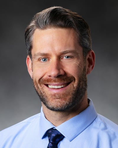 Samuel Doniach, APRN, CRNA smiling in front of a gray background.