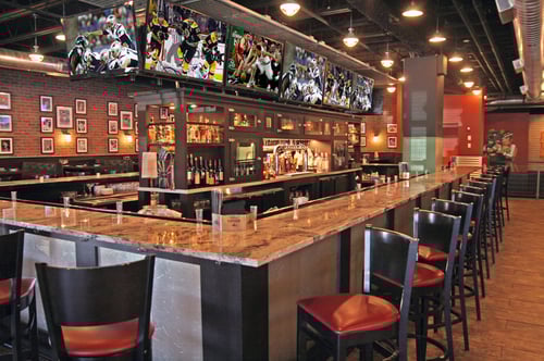 Large Bar area at SKYBOKX 109 Sports Bar & Grill in Natick, Massachusetts with Large TVS surrounding the bar to catch all the action. Booth seating in the background.