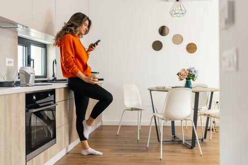 Woman standing in kitchen looking at phone