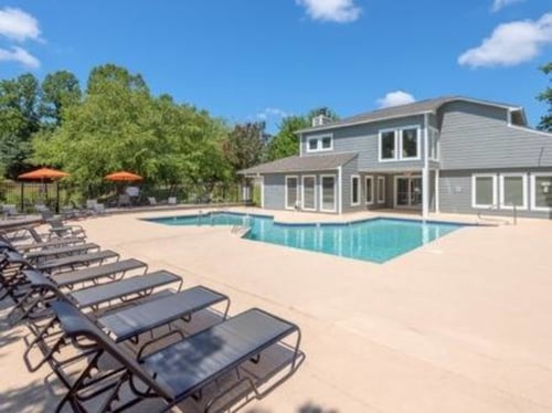 Apartment complex swimming pool with lounge chairs and a gray building under a blue sky.
