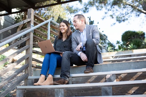 Smiling co-workers sitting on stairwell working on a laptop