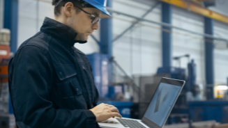 A man looking at a laptop inside an industrial warehouse.