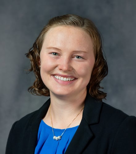 Mary is smiling in a bright blue blouse and black blazer.