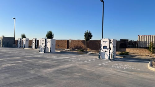 Several EVgo fast charging units installed in marked parking spaces at a public charging station, with EVgo logos on the chargers, protective bollards around each unit