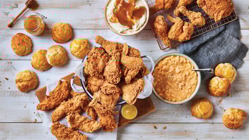Southern comfort food spread featuring crispy fried chicken, golden biscuits, creamy macaroni and cheese, and mashed potatoes with gravy, served on a rustic wooden table with honey on the side.