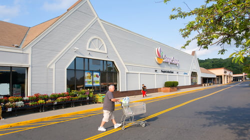 Man in shorts and grey t-shirt pushing shopping cart in front of Stop & Shop at Waterbury Plaza shopping center