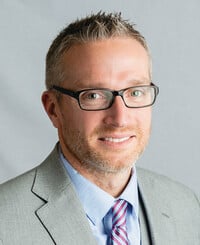 Agent Taylor Green standing and smiling wearing blue button up shirt with striped tie and gray blazer