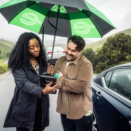 Enterprise employee helping Enterprise car rental customer roadside in the rain