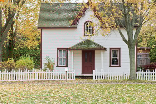 Charming cottage-style home surrounded by a white picket fence with colourful fall leaves on the lawn.