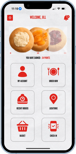 An iPhone with the kolache factory app screen. Buttons for checking in, ordering online, a location finder, redeeming points, and user information are visible