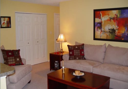 Furnished living room at Woodcrest Apartments with beige sofa, armchair, accent pillows, and wall art in Decatur, IL