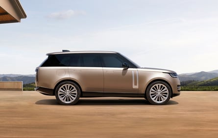 Side view of a champagne Range Rover parked with hills in the background.