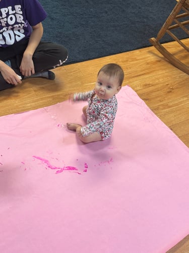 Infant exploring art on an art pad, making colorful marks with their hands.