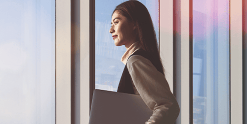 woman holding laptop looking out office window