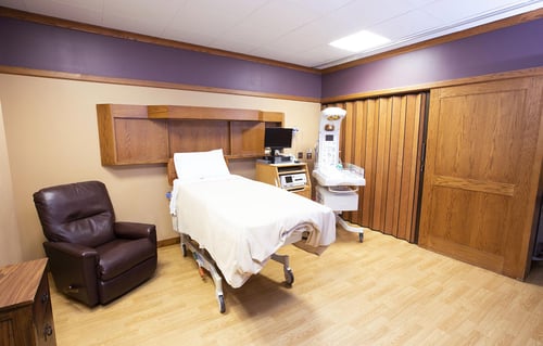 A view of a birthing room showing a birthing bed, recliner, infant warmer and monitoring equipment during labor.