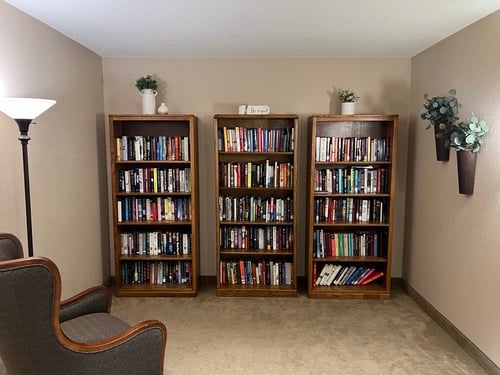 Three large wooden bookshelves filled with a variety of novels and non-fiction books in a quiet reading nook.