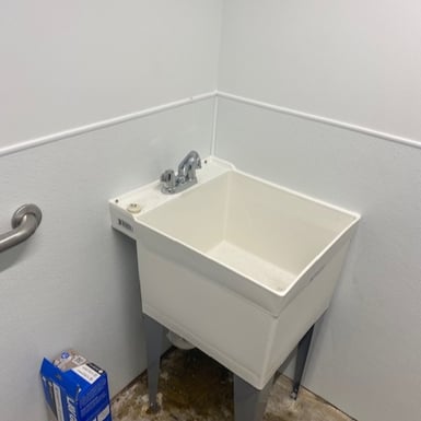 Commercial utility sink with faucet and plumbing connections in a service room, illustrating general plumbing installation and repair services.