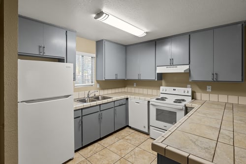 A kitchen with a white refrigerator, white oven, and grey cabinets. at Cedar Park Apartments, Chico, CA, 95926