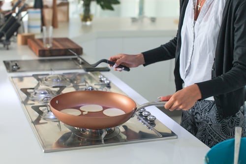 A woman cooks pancakes on an propane stovetop.