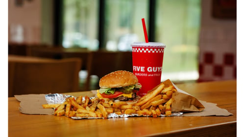 A Five Guys cheeseburger, regular fry and soft drink sit on a table inside a Five Guys restaurant.