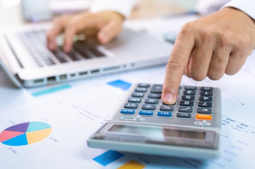 close up of hands on calculator and laptop keyboard with printed charts on desk