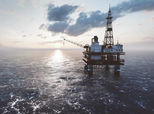 Offshore oil drilling platform in open ocean with tall derrick tower and crane.