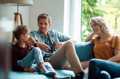 Son talking with mother and father sitting on sofa in living room