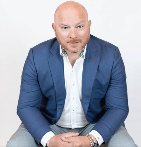 Agent Daniel Garbarino sitting and smiling wearing white button up shirt with navy blue blazer and gray pants