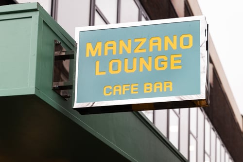 Manzano Lounge Cafe Bar written in yellow letters on a rectangular blue sign