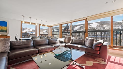 The luxurious living room with a large couch and windows looking out to the snow-covered town and mountains at Vail Spa Condominiums
