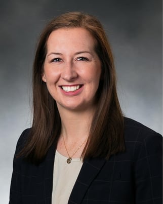 Laura Enright smiling in front of a gray background.