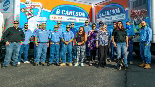 The B Carlson Heating, Cooling, and Plumbing team standing in front of their trucks.