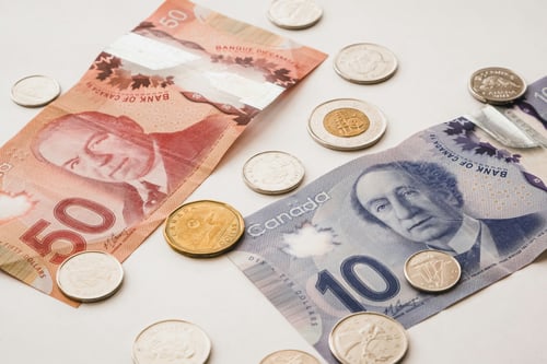 Top-down flat lay of Canadian currency — a red $50 bill and a purple $10 bill with scattered coins on a white background.