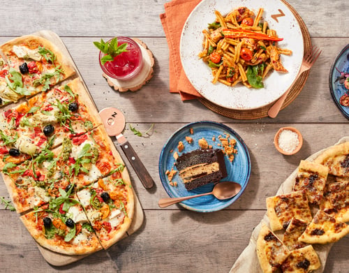 Feast shot consisting of pizza, pasta, dessert and cocktail.