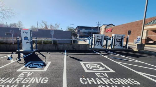 Several EVgo fast charging units installed in marked parking spaces at a public charging station, with EVgo logos on the chargers, protective bollards around each unit.