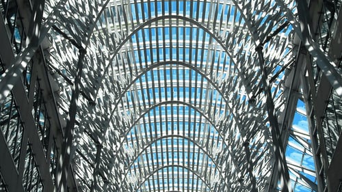 An intricate architectural ceiling with a lattice pattern, allowing blue sky to filter through, casting dynamic shadows indoors.