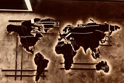 Decorative metal world map wall art with warm LED backlighting, mounted on a textured concrete wall.