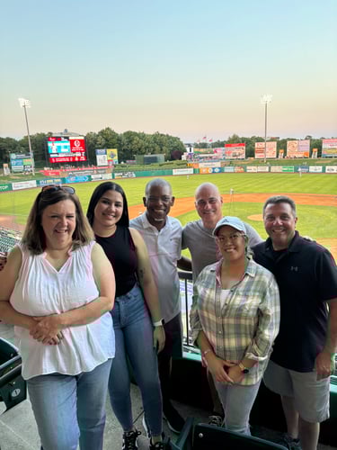 Agent Lenny and five team members standing and smiling together at baseball game for Summer Office Event