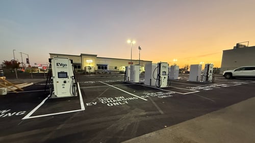 Several EVgo fast-charging units installed in marked parking spaces at a public charging station, with EVgo logos on the chargers, protective bollards around each unit