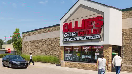 Black car passing by Ollie's as two men walk in