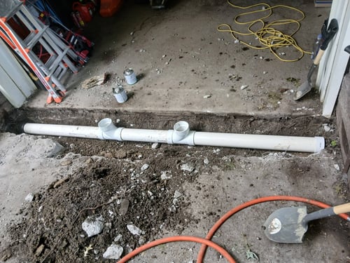 Exposed PVC pipe and two open cleanout fittings at a garage threshold during Bluefrog work.