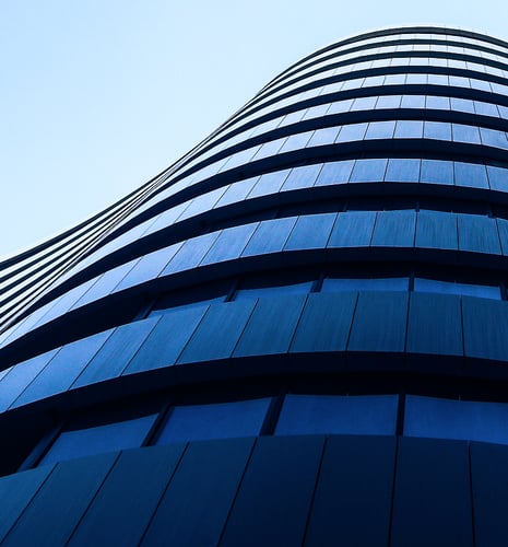 Curved modern skyscraper with reflective blue glass panels against a clear sky. The sleek, upward perspective evokes a sense of innovation.