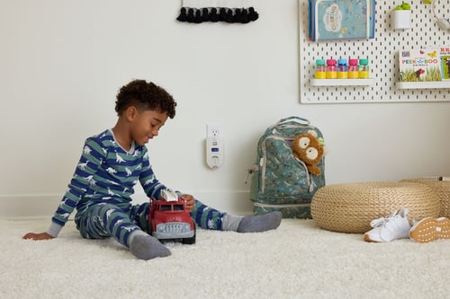 A boy plays with a toy truck, behind him a Kidde Carbon Monoxide Alarm with Indoor Air Quality Monitoring.