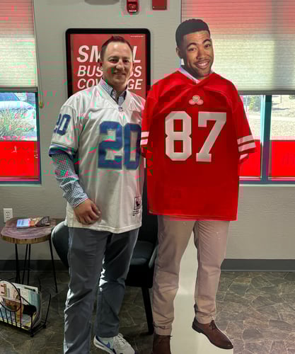 Agent in a blue and whte jersey standing next to a card board cut out of jake from state farm who is also wearing a red jersey.