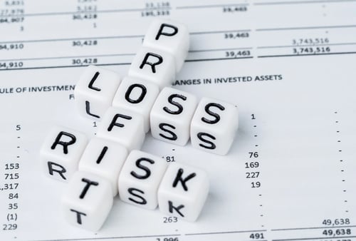 Cubes spelling "PROFIT," "LOSS," and "RISK" rest on a financial document. The arrangement suggests the balance of financial concepts.