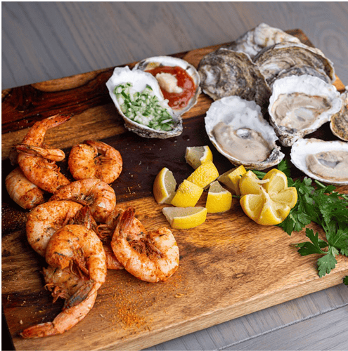 Platter of fresh shrimp and raw oysters from Outer Banks Steamers with lemon wedge and cocktail sauce.