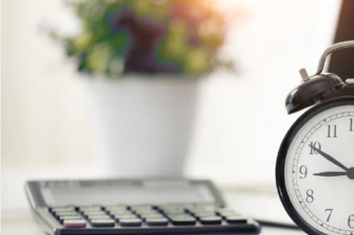 Close-up of table with a calculator, clock, and houseplant.