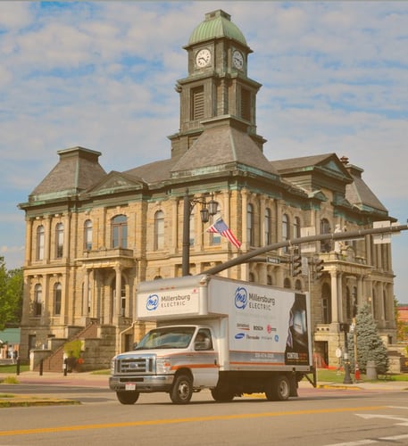 Millersburg Electric branded delivery truck parked in front of a historic courthouse.