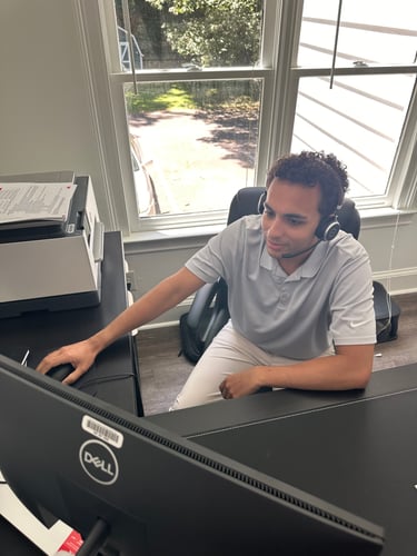 Man with headset on answering phone calls and sitting at desk on computer in office