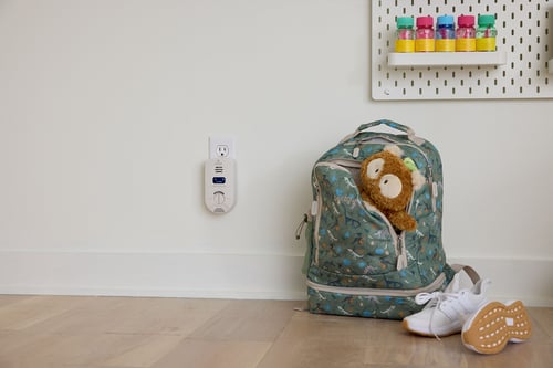 Kidde carbon monoxide detector on wall next to a child's backpack.